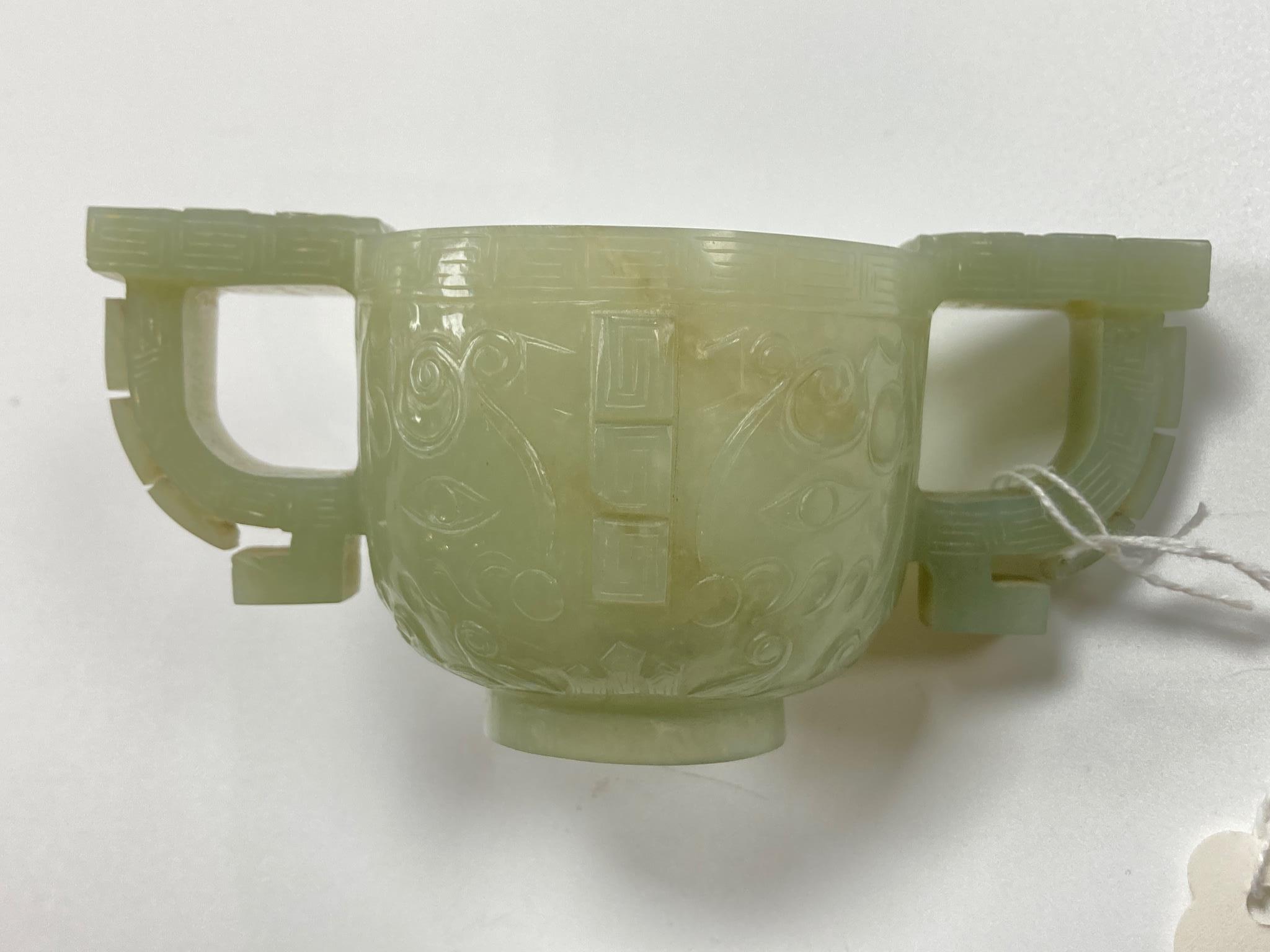 A Chinese archaistic celadon jade two handled cup, 17th century, 12.9cm across 6.1cm high, associated wood stand